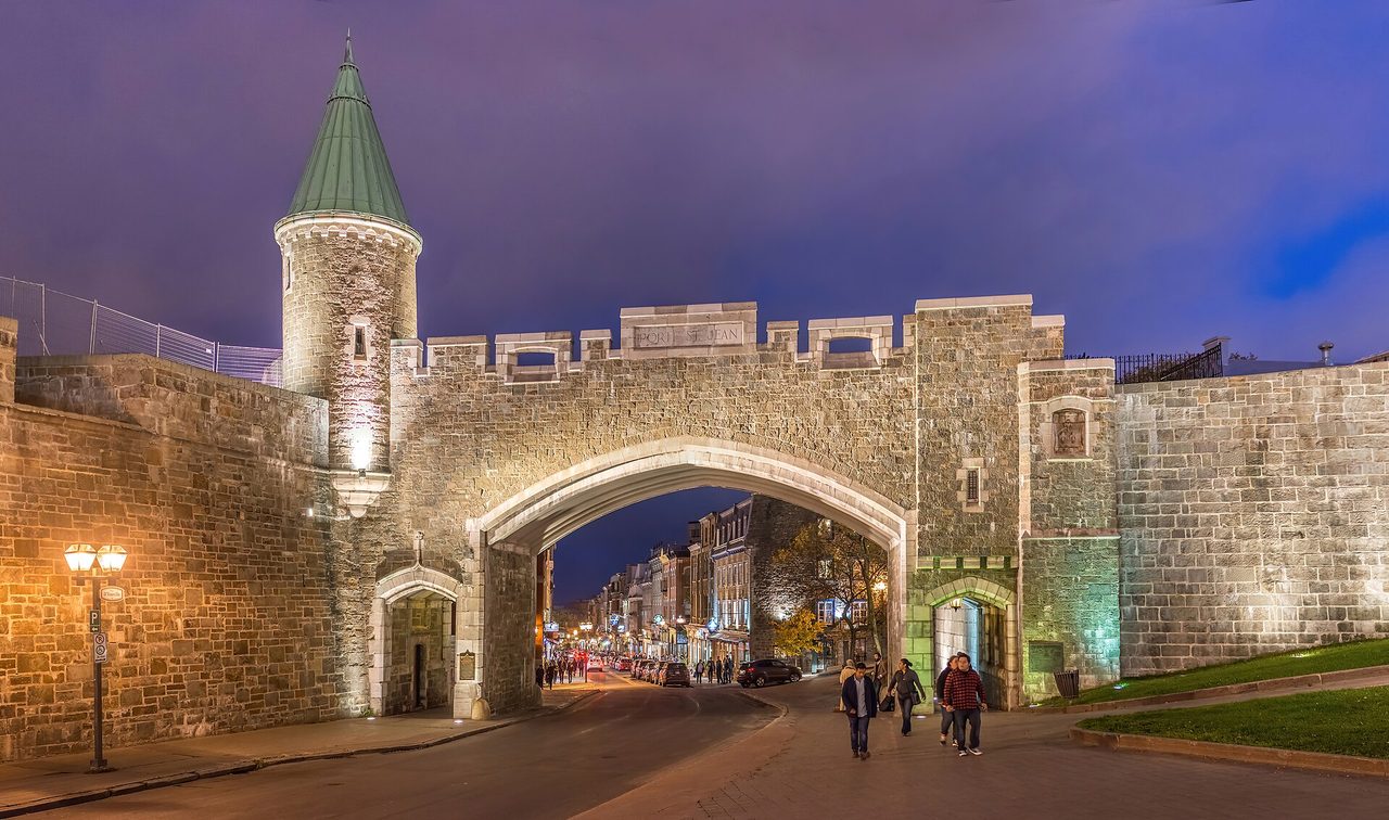 The illuminated Porte Saint-Jean gate in Quebec City's stone fortifications at dusk