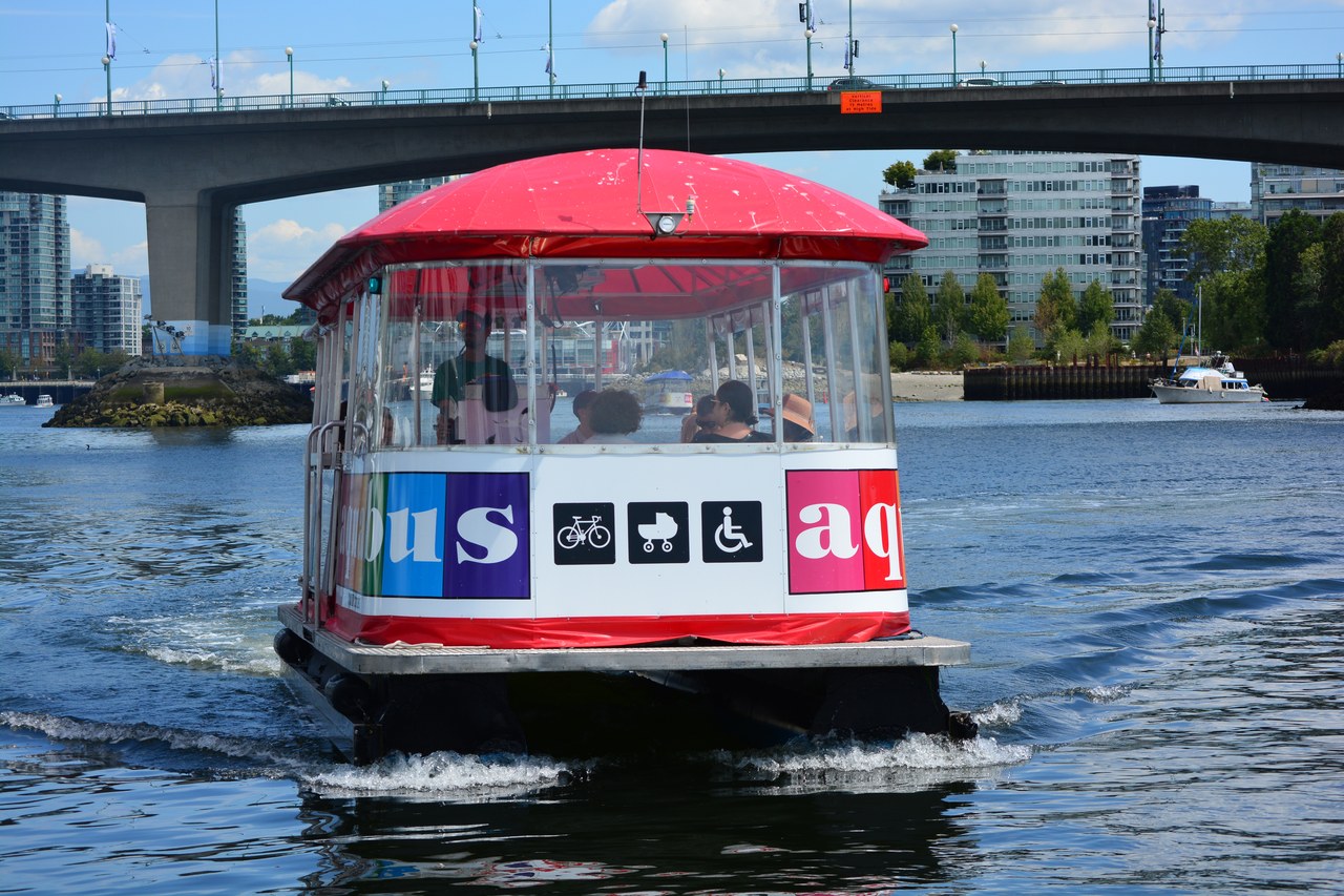 A colorful Aquabus ferry crossing False Creek with the Cambie Street Bridge behind it