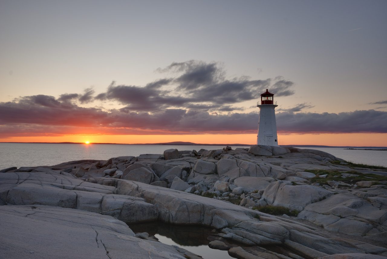 Peggy's Point Lighthouse glowing at sunset on the granite rocks of Peggy's Cove