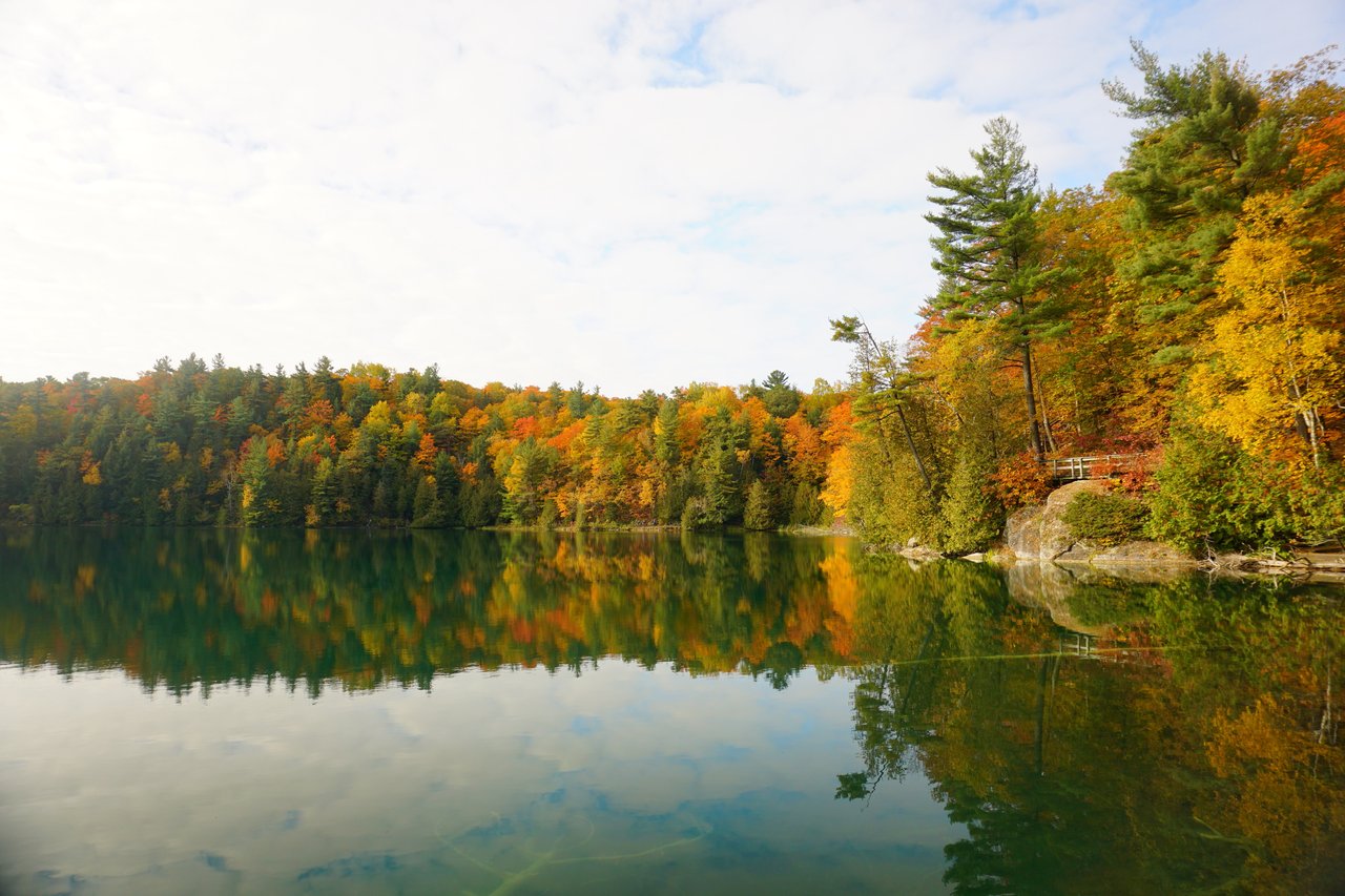 Pink Lake's calm turquoise water reflecting autumn foliage in Gatineau Park