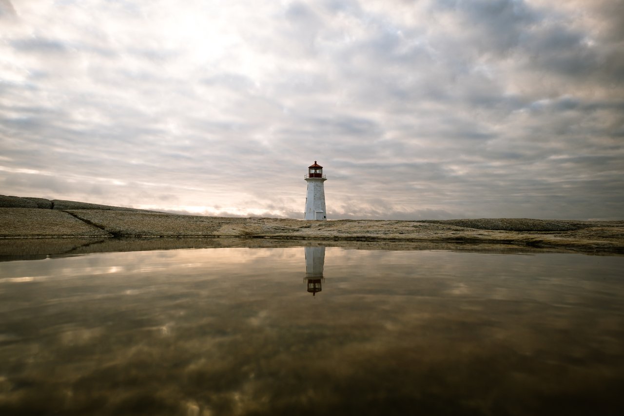 Peggys Point Lighthouse standing on granite rocks and reflected in a tide pool at Peggy's Cove, Nova Scotia
