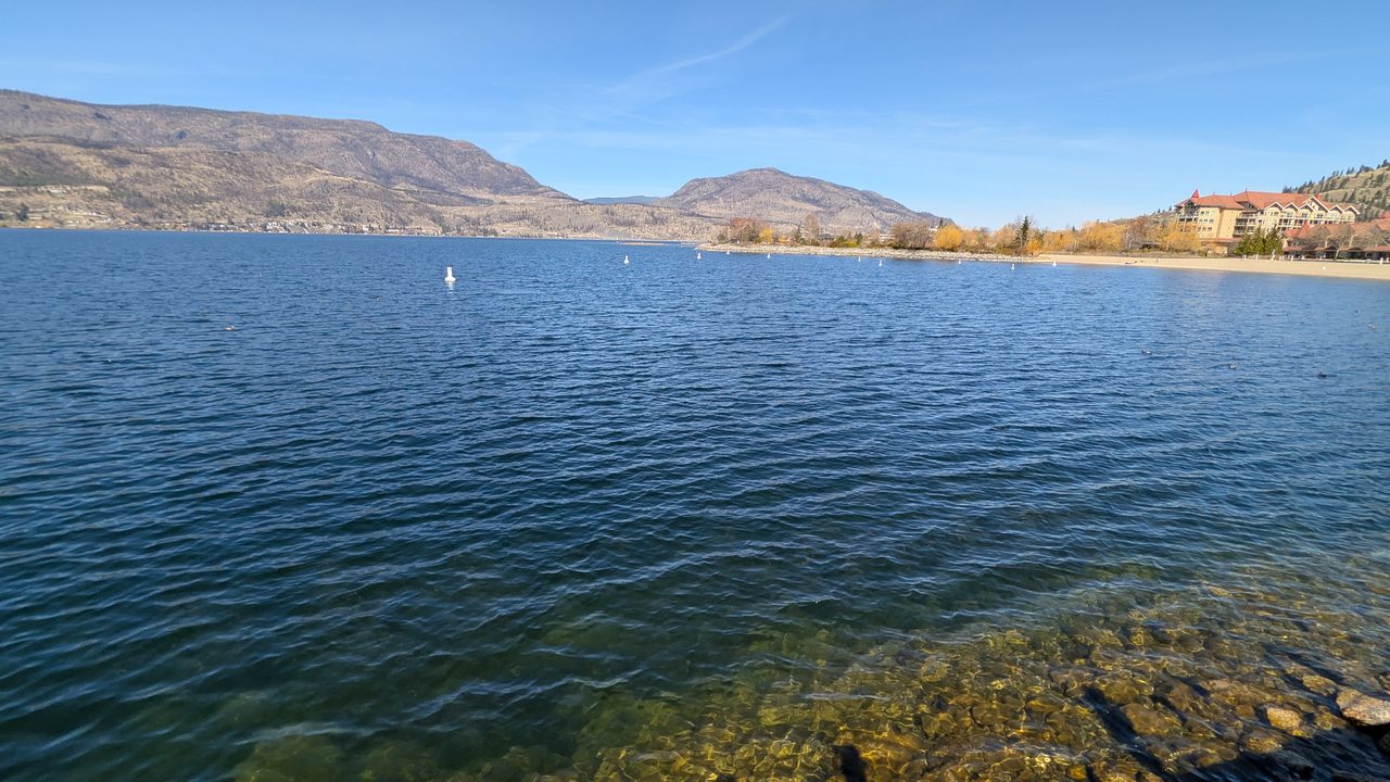 Okanagan Lake glittering under a summer sky, with hills rising beyond Kelowna's shoreline