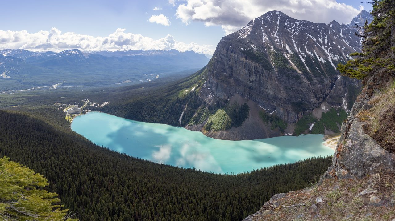 Panoramic view over the turquoise waters of Lake Louise surrounded by forested Rocky Mountain peaks in Banff National Park