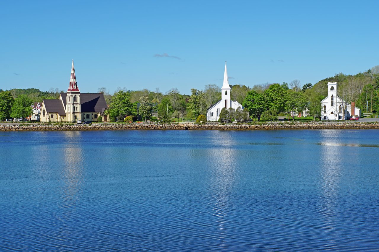 The three historic churches of Mahone Bay reflected along the shoreline at golden hour