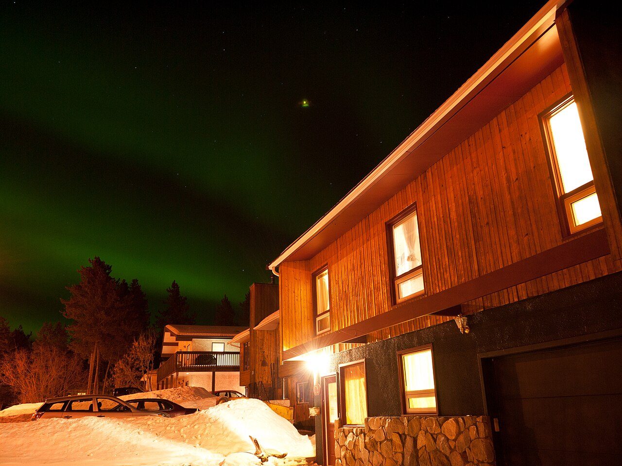 Green aurora borealis glowing over a snowy street in Whitehorse, Yukon, on a clear winter night
