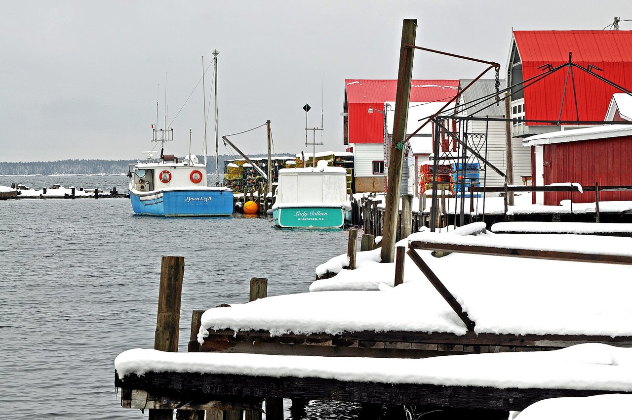 A snow-covered fishing harbour in Lunenburg County, Nova Scotia in winter with boats docked in icy water