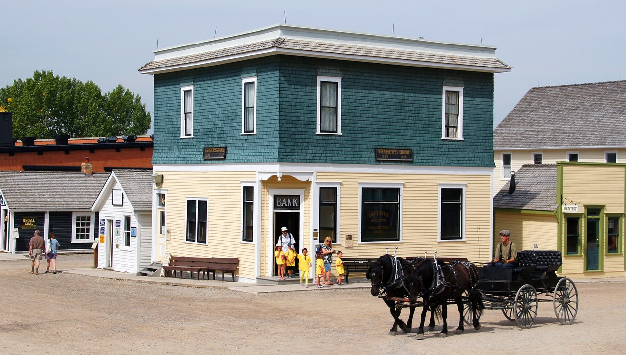 Horse-drawn carriage and costumed interpreters outside the bank building in Heritage Park Historical Village on a summer day