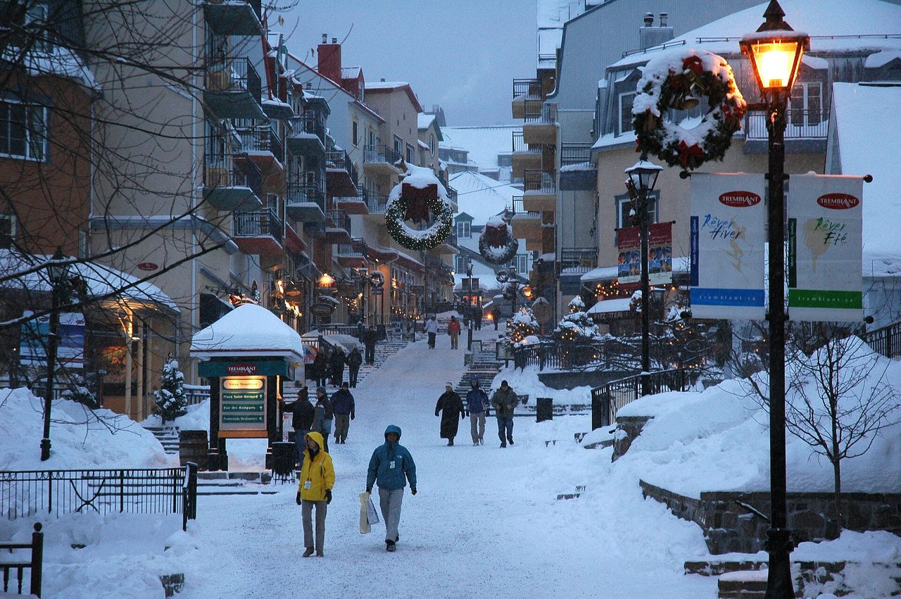Colourful pedestrian village of Mont-Tremblant glowing at dusk with ski slopes behind