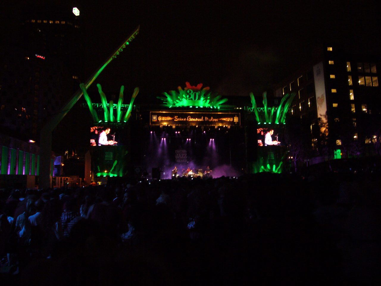 The main stage lit up in green at night during the Montreal International Jazz Festival, with a crowd gathered in front