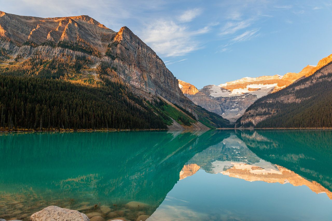 Turquoise Lake Louise at sunrise with the Victoria Glacier behind and red canoes lined up on the shore