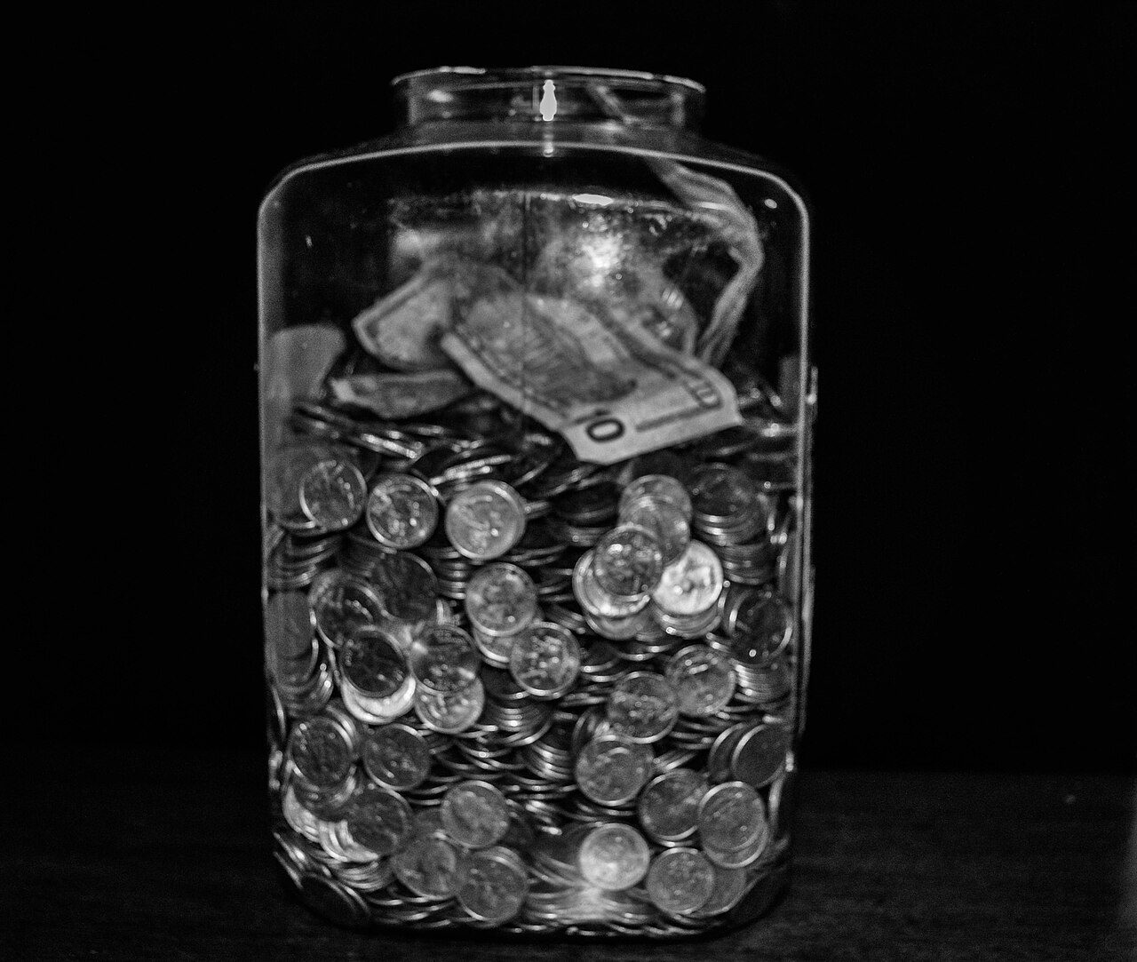 Glass tip jar filled with coins and folded bills on a counter