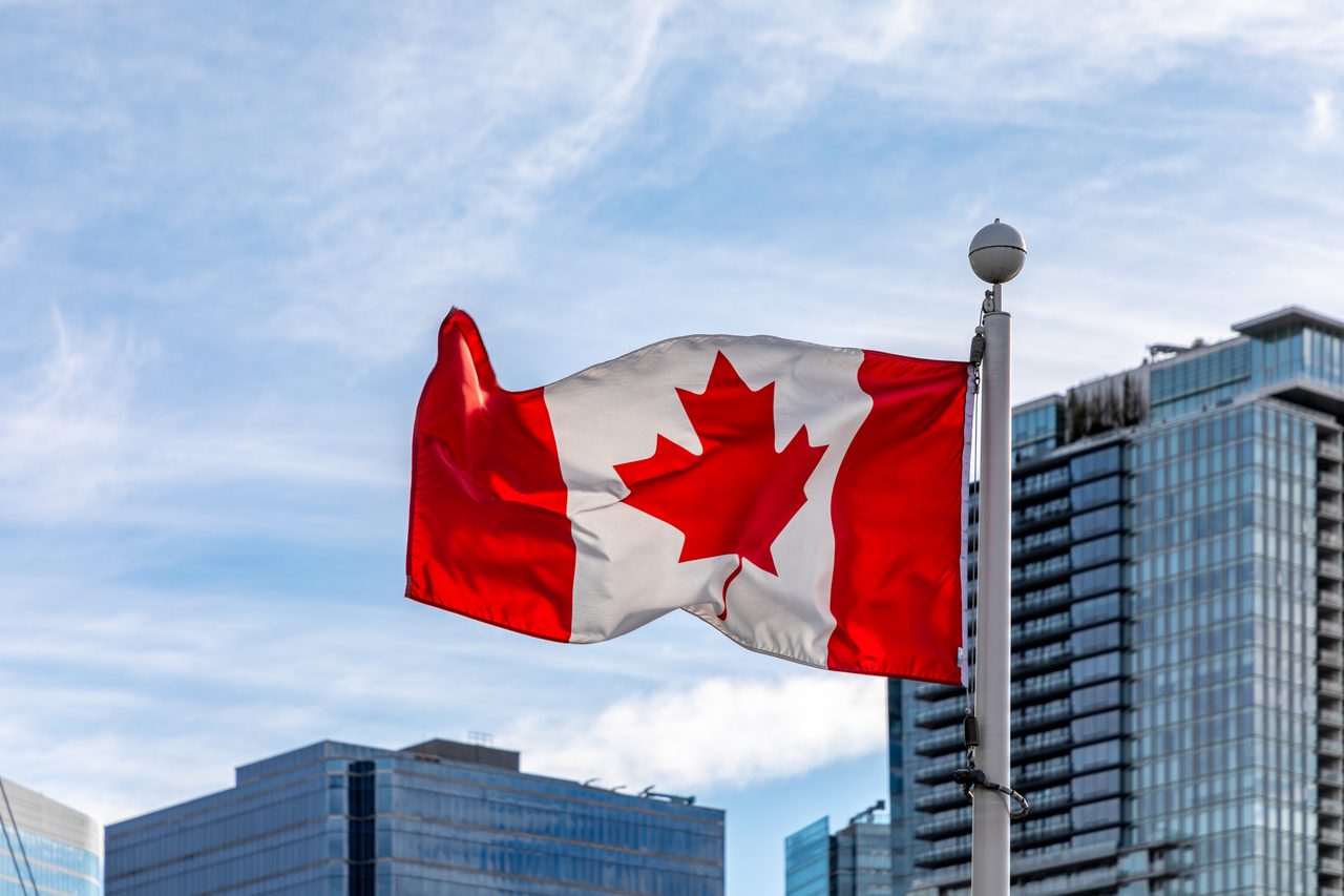 Large Canadian flag waving at Canada Place in Vancouver with the harbour behind it