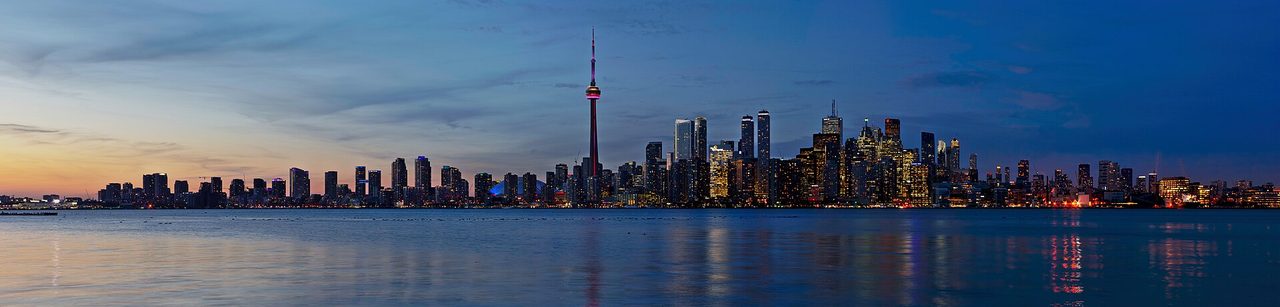 Toronto skyline at sunset with the CN Tower glowing against pink and orange clouds, viewed across Lake Ontario from the Toronto Islands