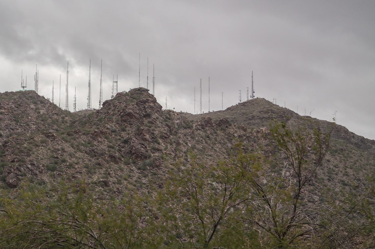 A cell phone tower standing on a grassy hillside under a cloudy sky
