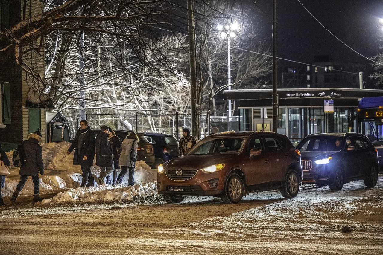 Pedestrians in winter coats crossing a snow-covered street in Quebec City at night under falling snow