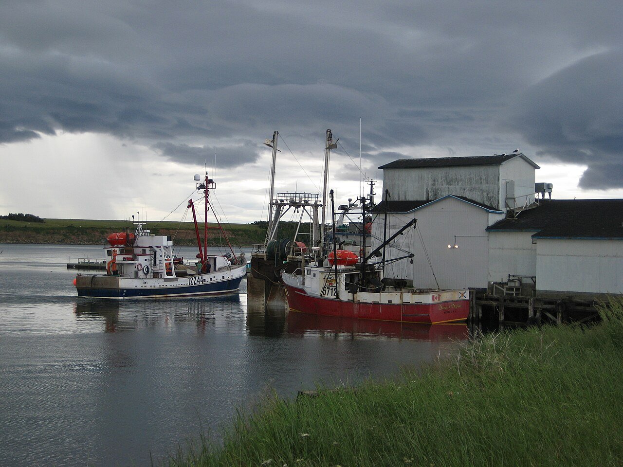 Fishing boats moored at the wharf in Chéticamp harbour under stormy autumn skies