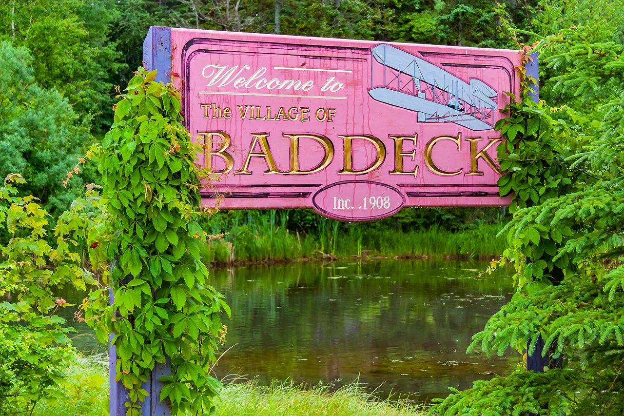 Baddeck waterfront on the calm Bras d'Or Lake with sailboats and village buildings along the shore