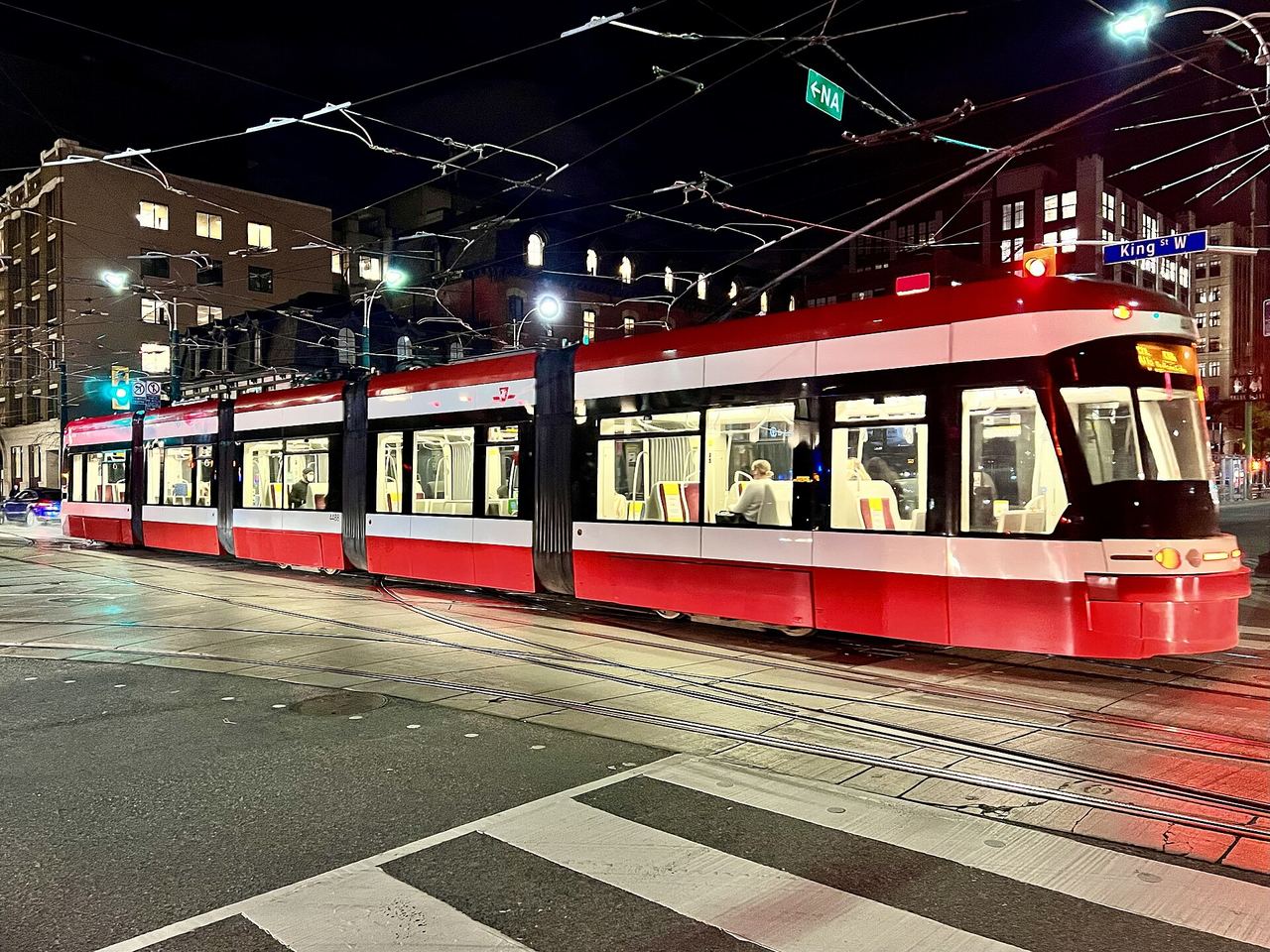 A red Toronto streetcar at night on the tracks at Spadina and King