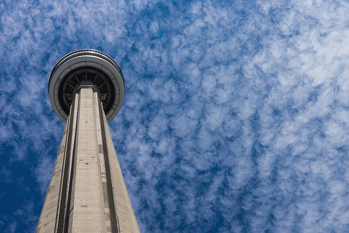 The CN Tower rising above downtown Toronto's office towers, seen from street level on a clear day