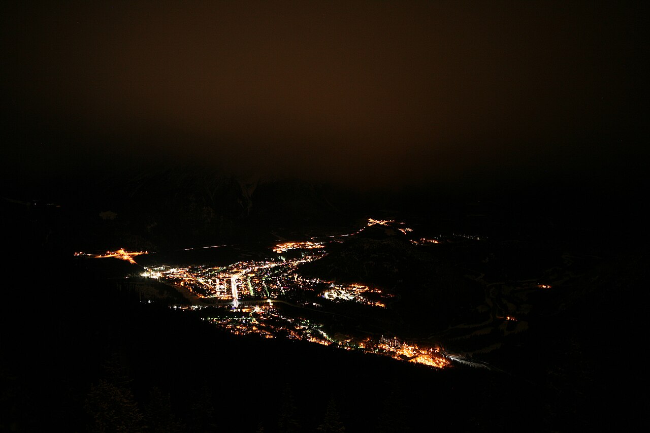 Banff townsite glowing at night, ringed by snow-covered Rocky Mountain peaks