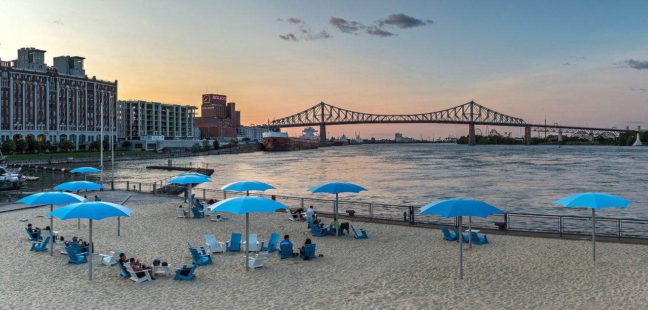 Sunset over the Clock Tower Beach at the Old Port, with blue umbrellas on the sand and the Jacques-Cartier Bridge in the distance
