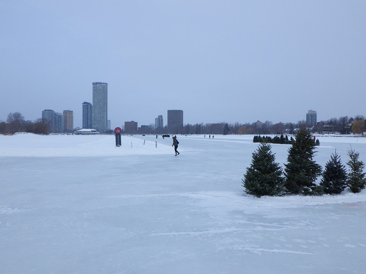 Skaters gliding along the frozen Rideau Canal Skateway in winter, with the city skyline behind them