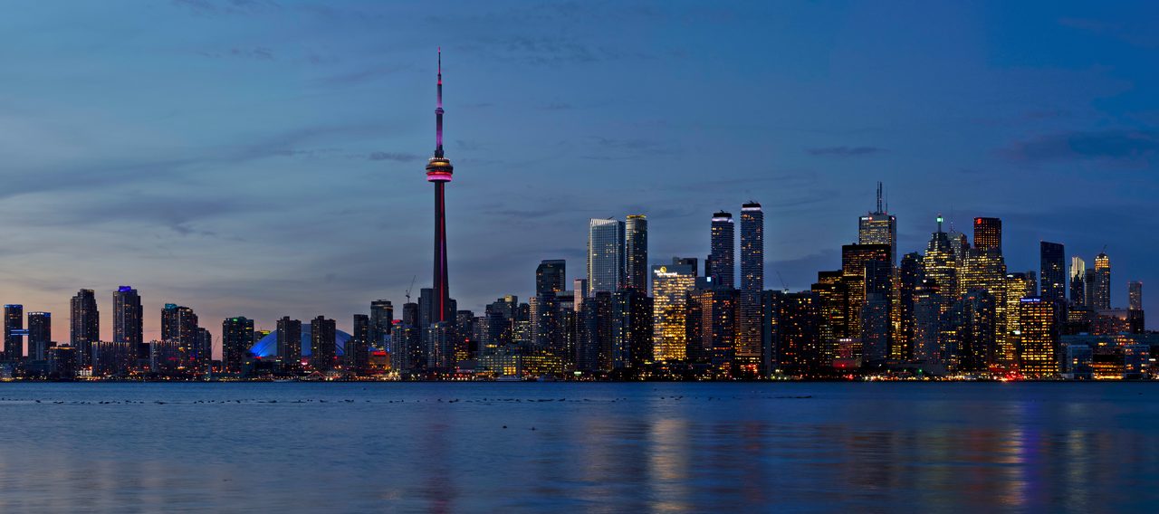 Toronto skyline at sunset seen across Lake Ontario, with the CN Tower rising above the downtown towers