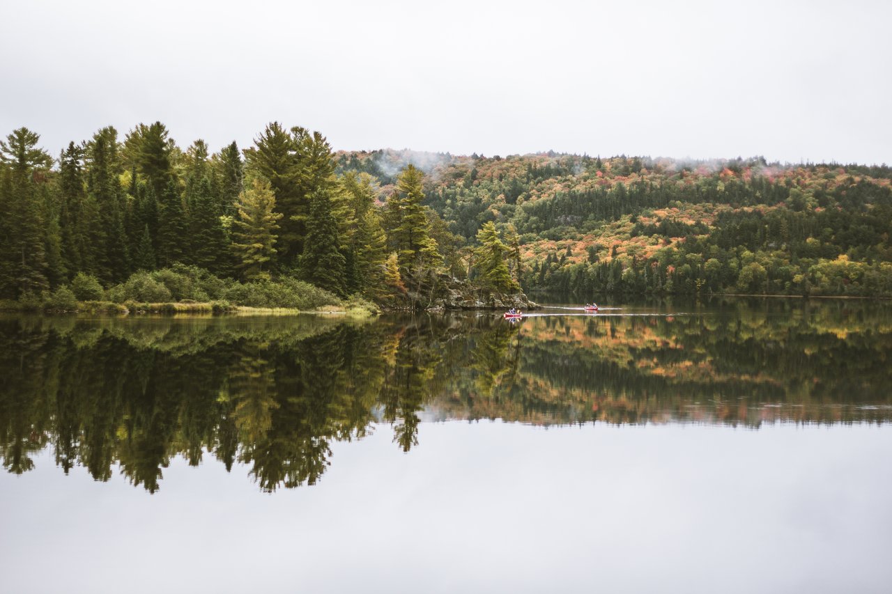 Canoe on a calm autumn lake ringed by red and orange fall trees