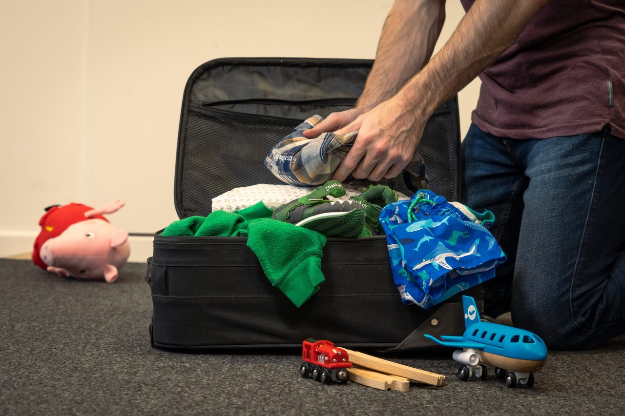 Hands packing folded clothes into an open suitcase on a bed before a trip to Canada