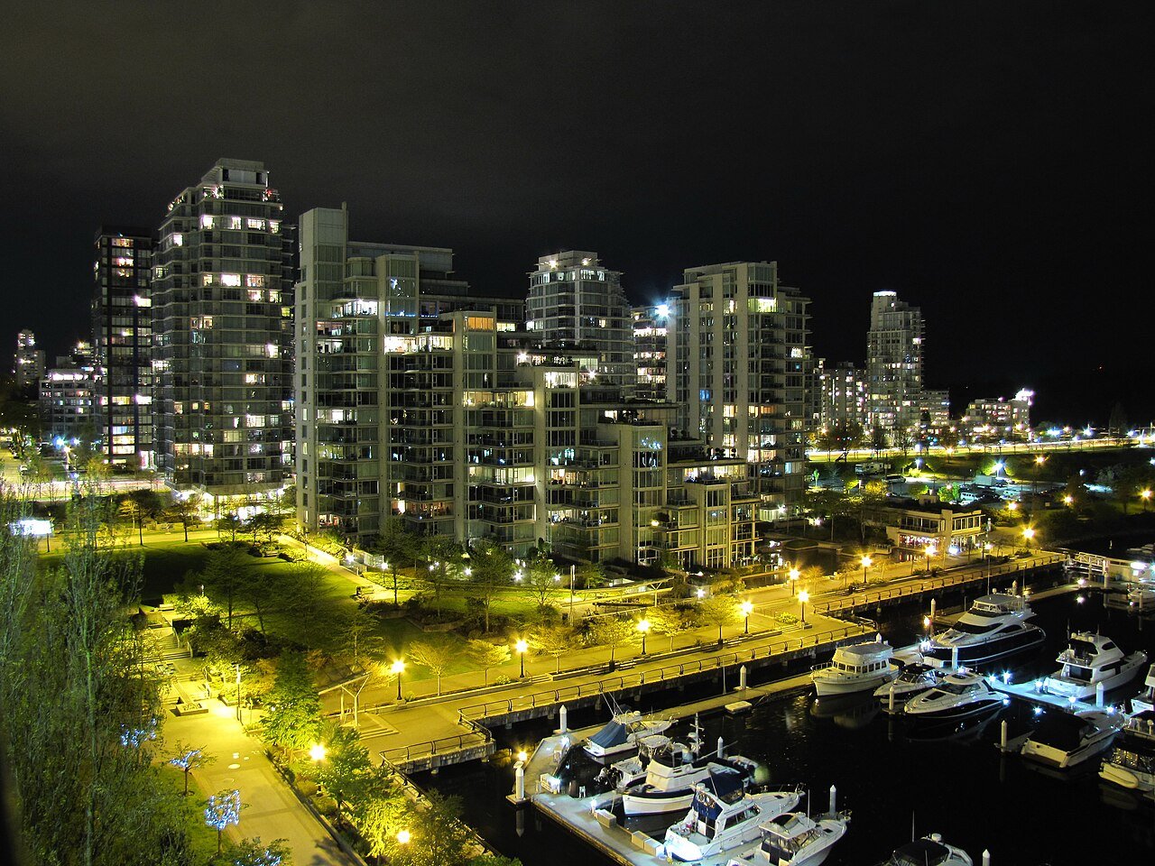 Glass condo towers and sailboats lit up at night along the Coal Harbour marina in Vancouver