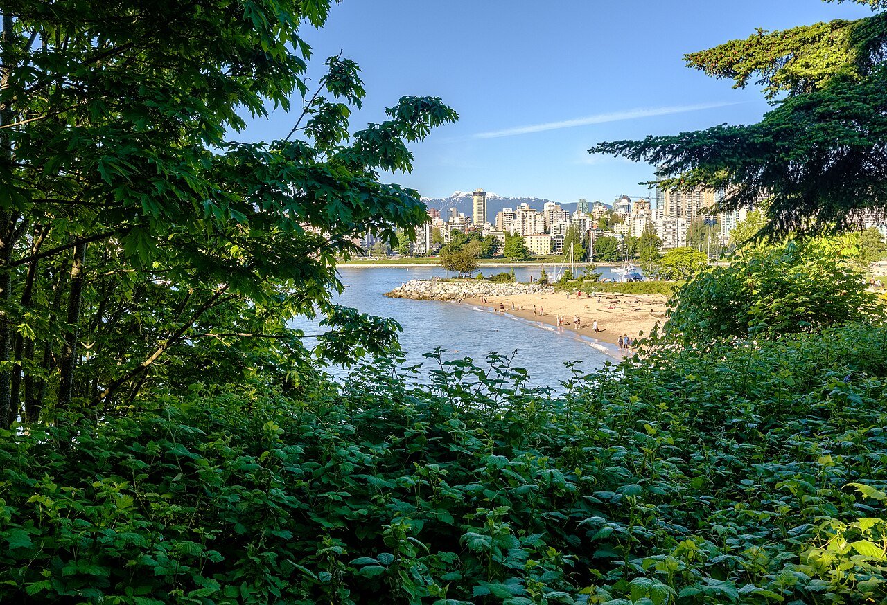 Kitsilano Beach seen through green trees with the downtown Vancouver skyline behind
